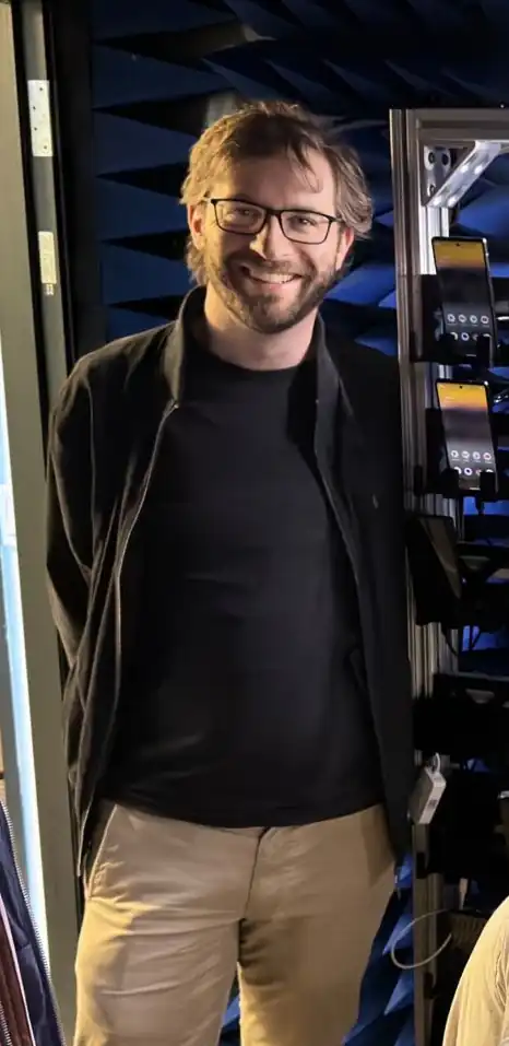 Photo of the author leaning against a metal rack containing rows of Android smartphones